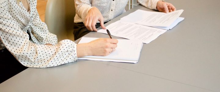 woman signing on white printer paper beside woman about to touch the documents